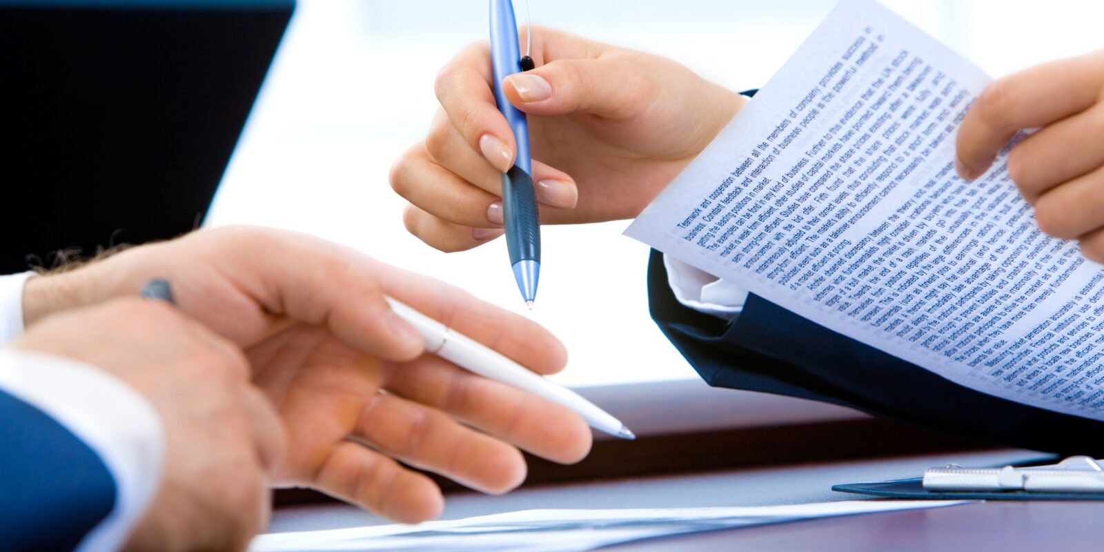 Mãos de duas pessoas, segurando folhas contratuais, aparentemente dialogando sobre um contrato