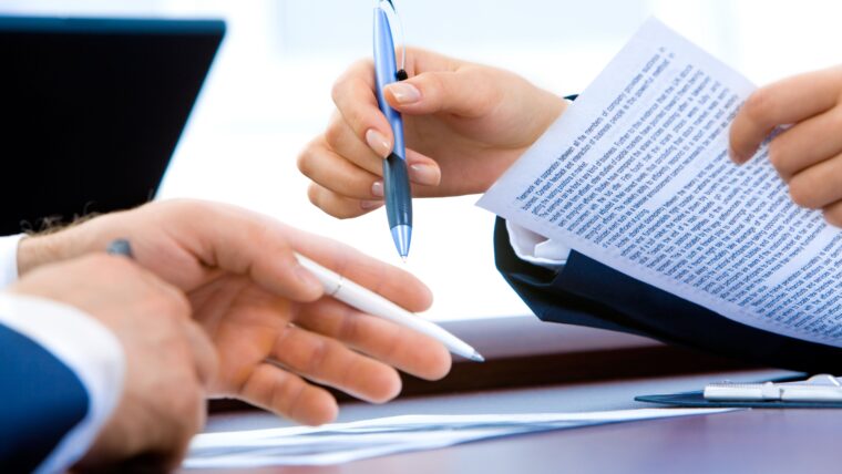 Mãos de duas pessoas, segurando folhas contratuais, aparentemente dialogando sobre um contrato