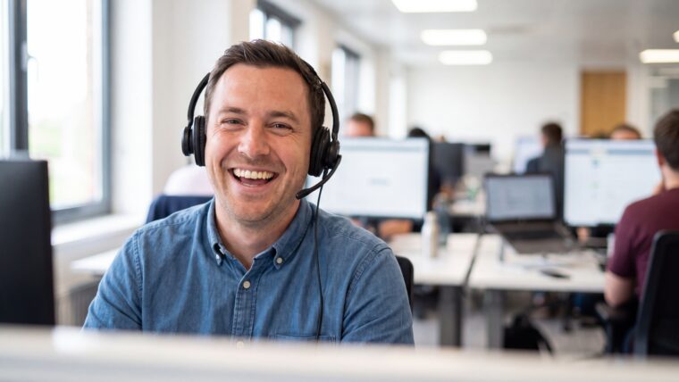 Retrato de um atendente de call center alegre, usando headset enquanto presta assistência a clientes em um escritório moderno e movimentado.